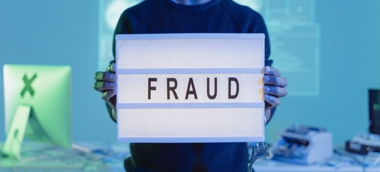 a man in a black sweater holding a sign that says "fraud"