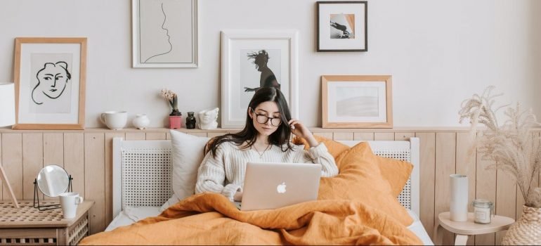 a woman lying on a big bed in her bedroom, looking at her lap top