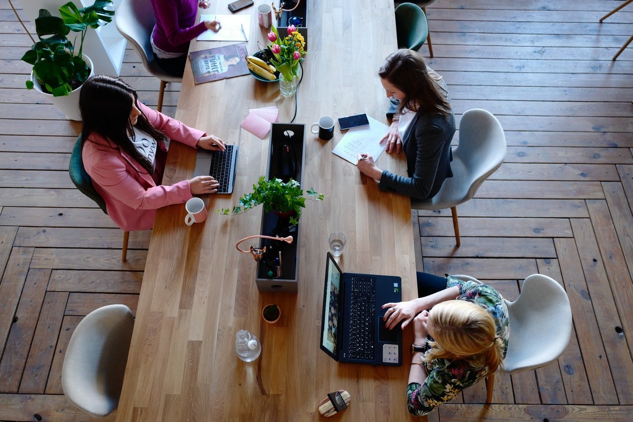 Three women sitting on white chairs in front of table working on laptops