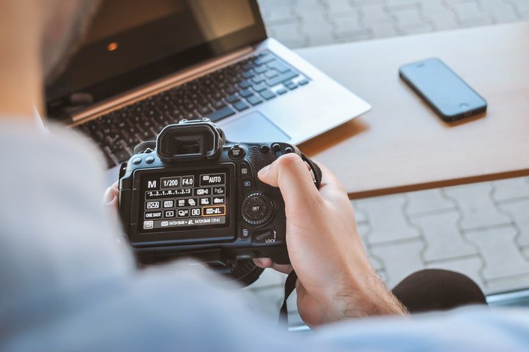 A faceless man looking at a camera in front of a laptop and a phone, thinking about what to photograph when moving house.