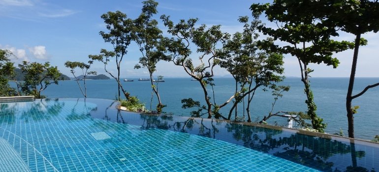 A swimming pool over the ocean, surrounded with trees.