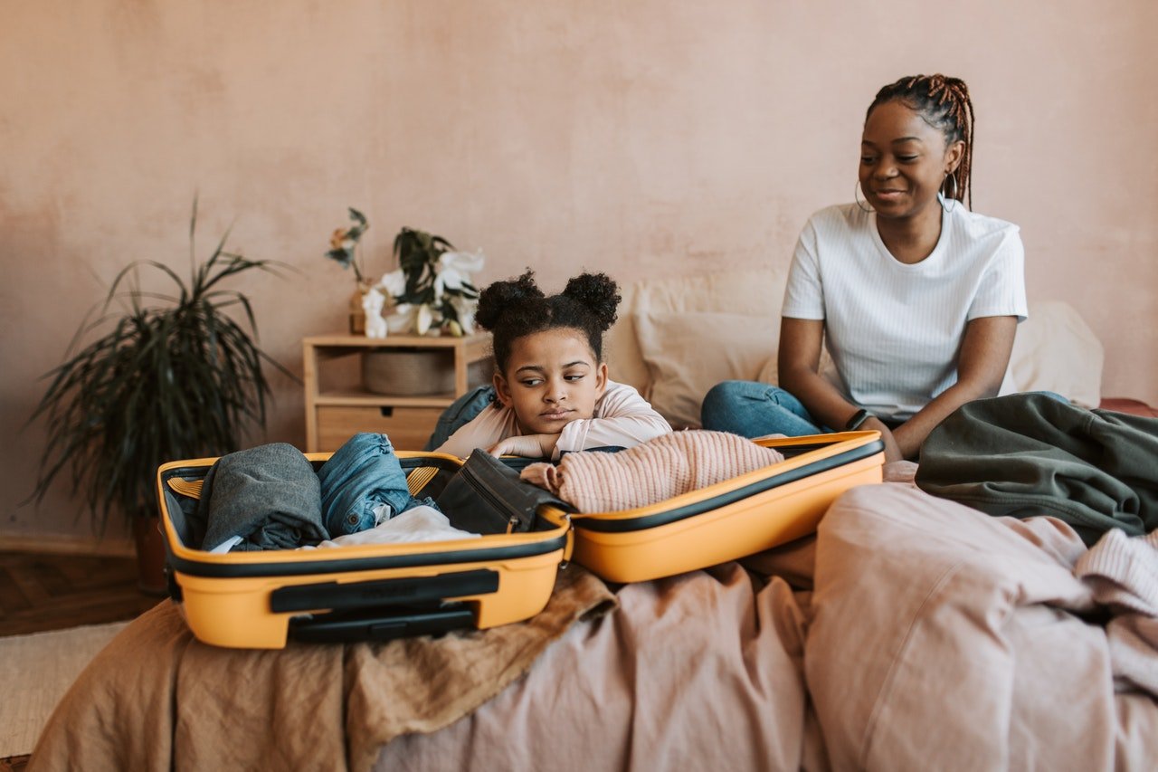 a mother and a daughter packing a suitcase on to organize kids' toys before moving