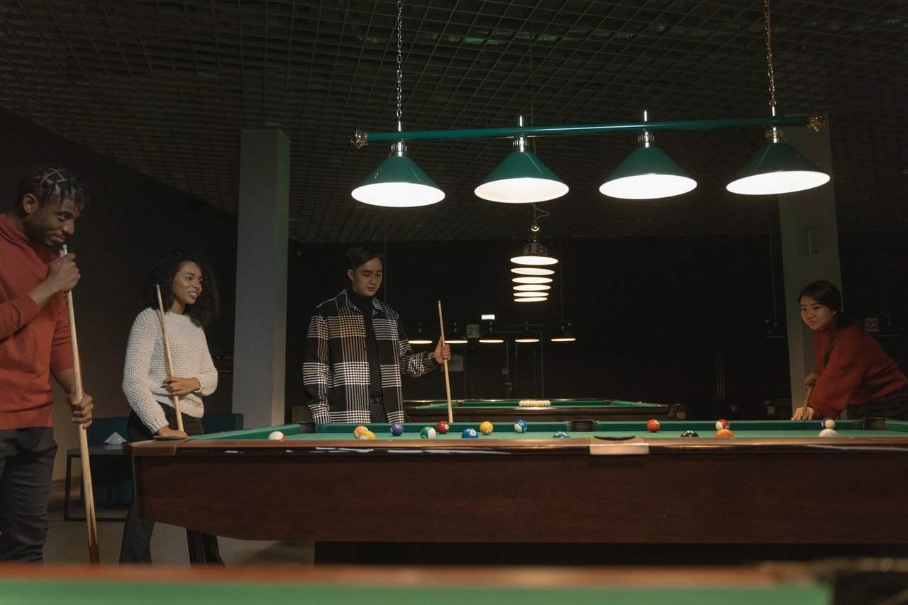 four people playing pool in a dark room