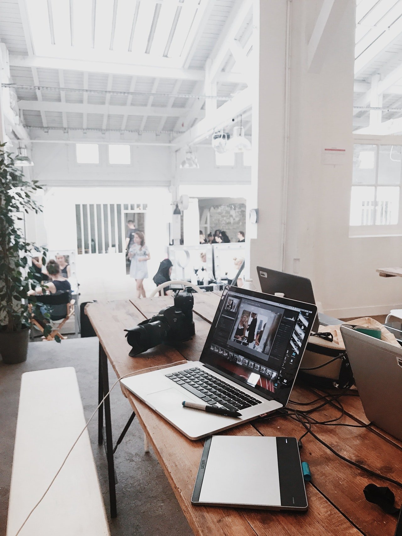 A laptop and a tablet on a table next to a camera