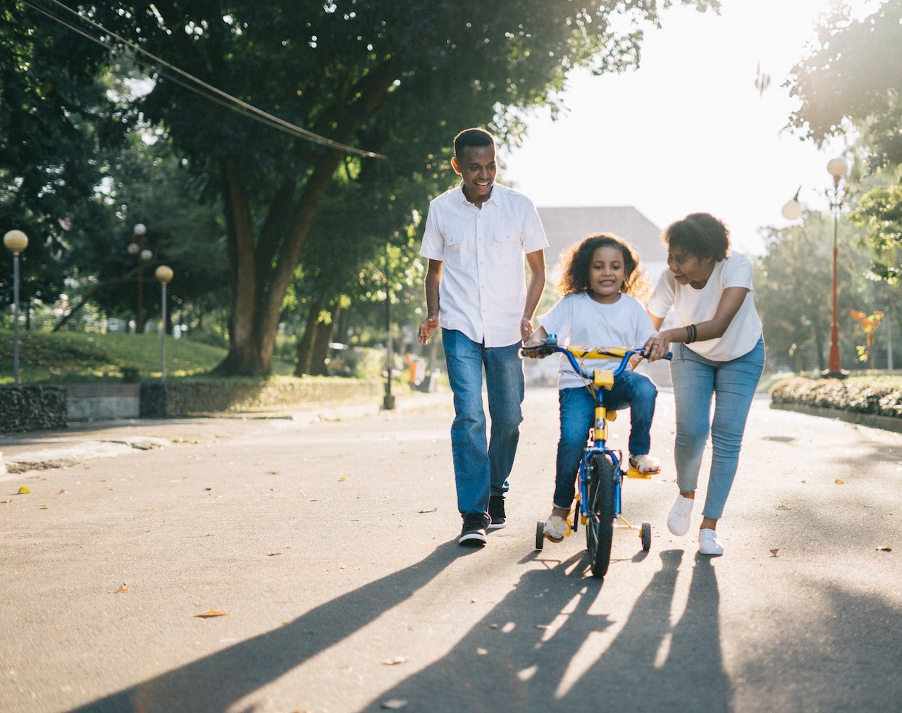 A man stands behind his wife, teaching his child on how to ride a bicycle