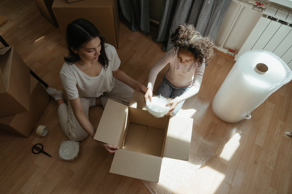 Woman and child sitting on the floor and packing fragile in the box, talking about what to do with packing supplies after moving to Gilroy