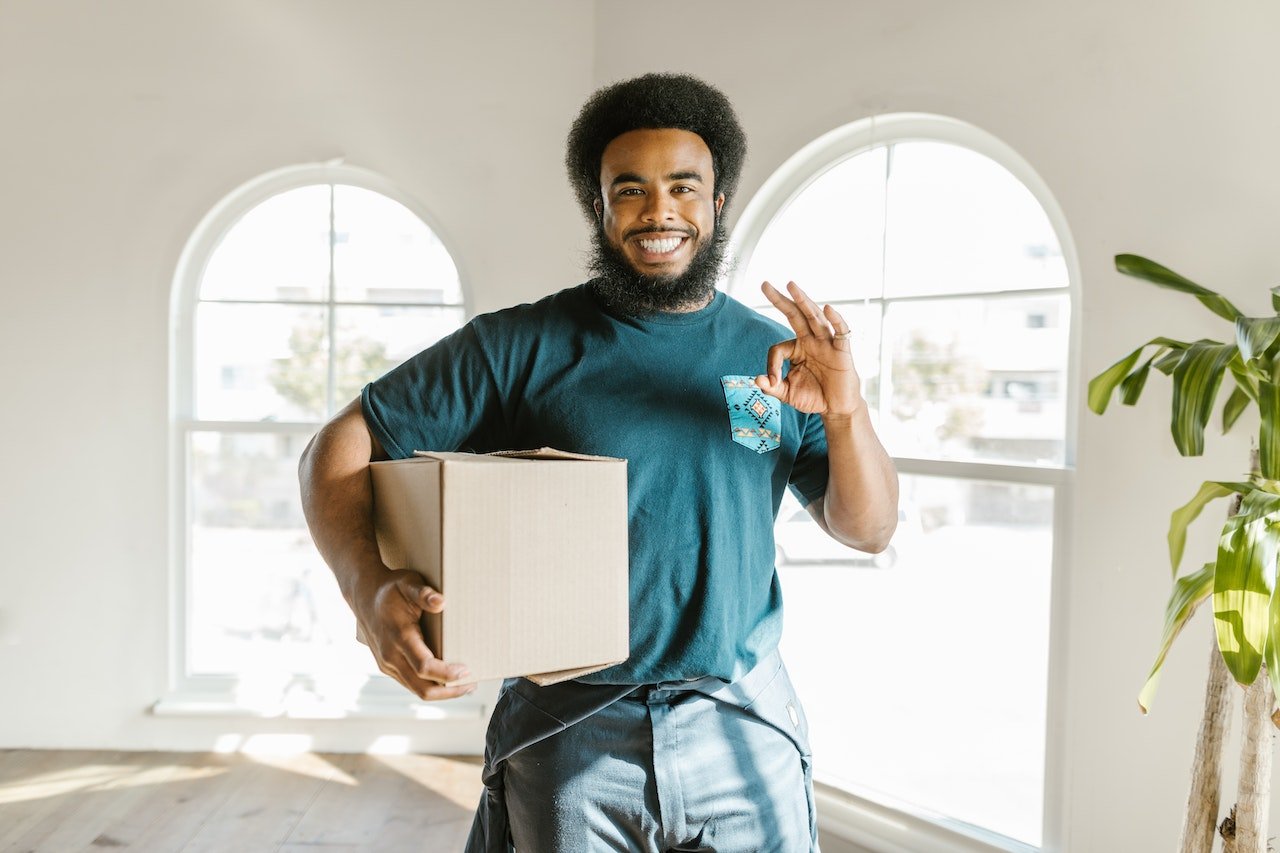 A professional mover holding a cardboard box, signing with his other hand