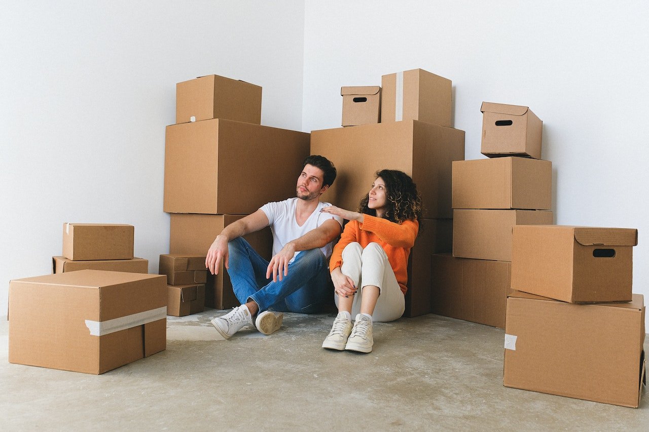a man and a woman sitting on the floor in front of cardboard boxes and talking about moving from Watsonville to Saratoga