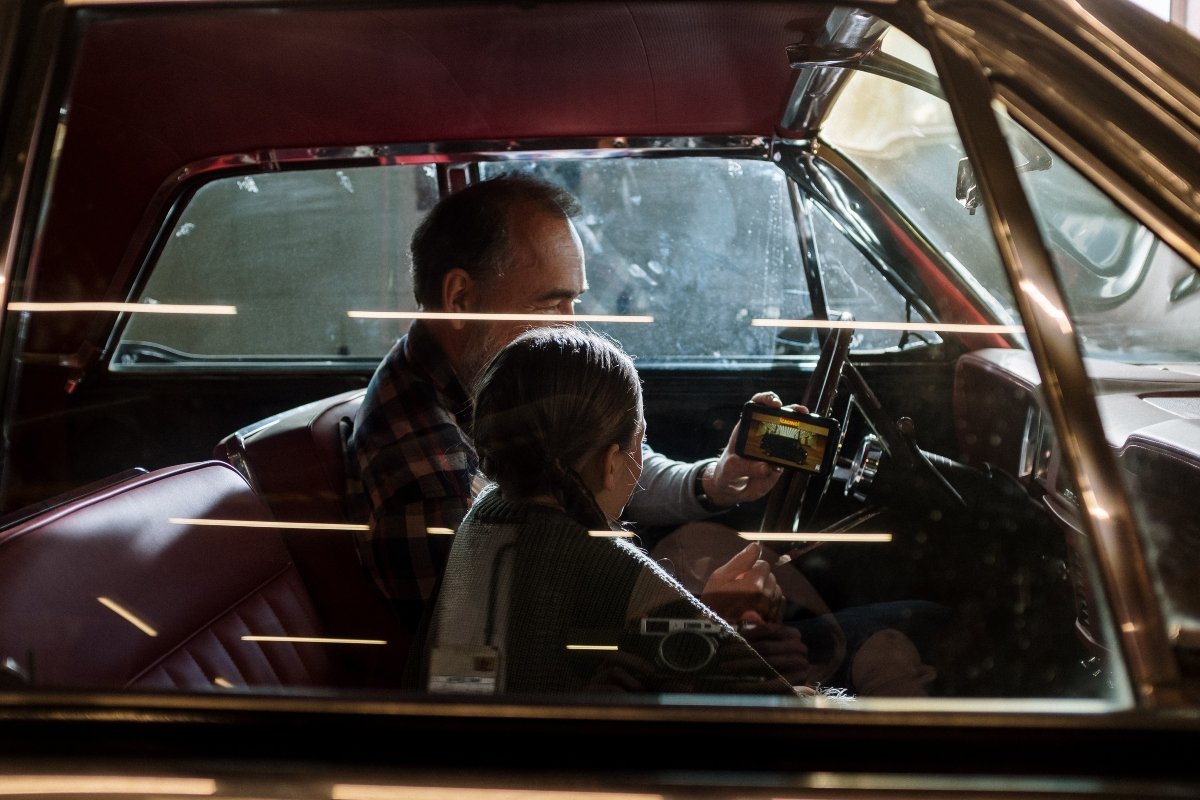 A man and the girl sitting in the car and looking at his smartphone