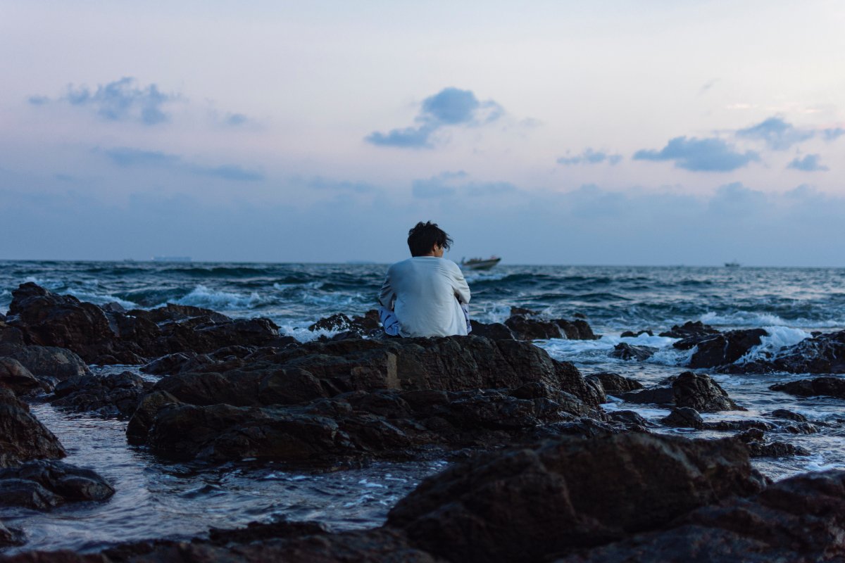 an alone person sitting on the stone on the seashore
