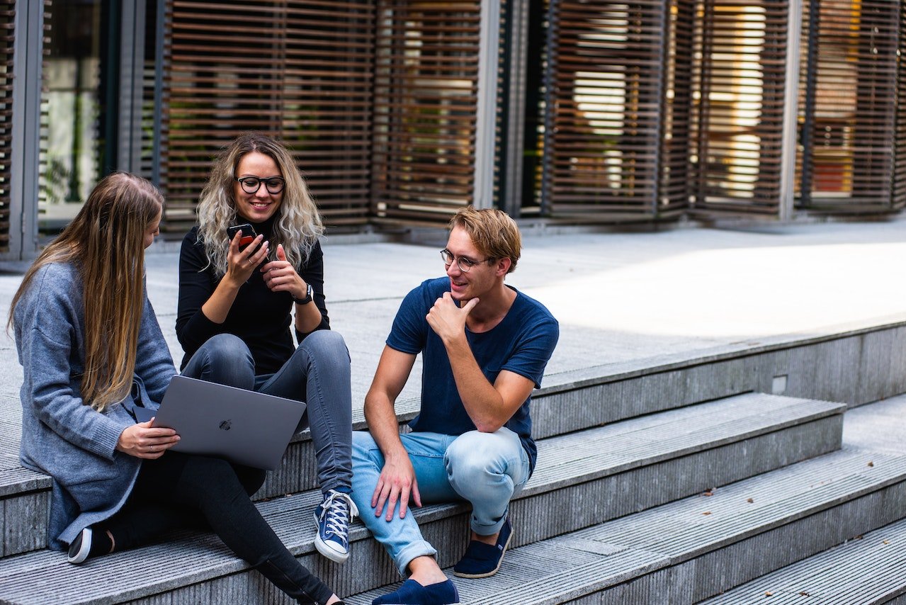 Three people are sitting on the steps and talking about top California Cities for college grads.