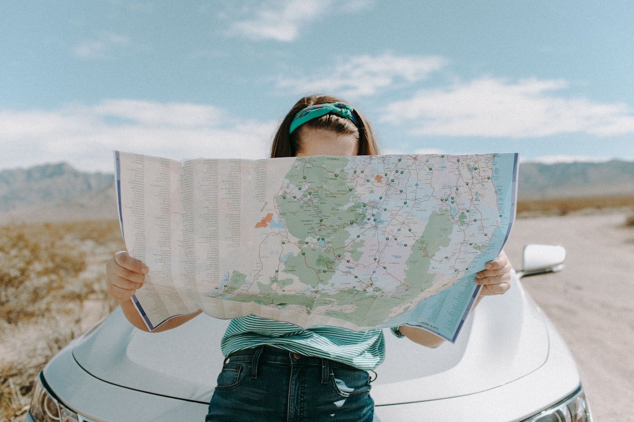 a woman sitting on a car and reading map