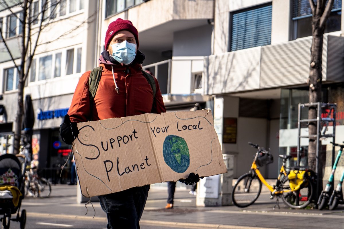A man with a medical mask on his face and a cardboard with an inscription in his hands