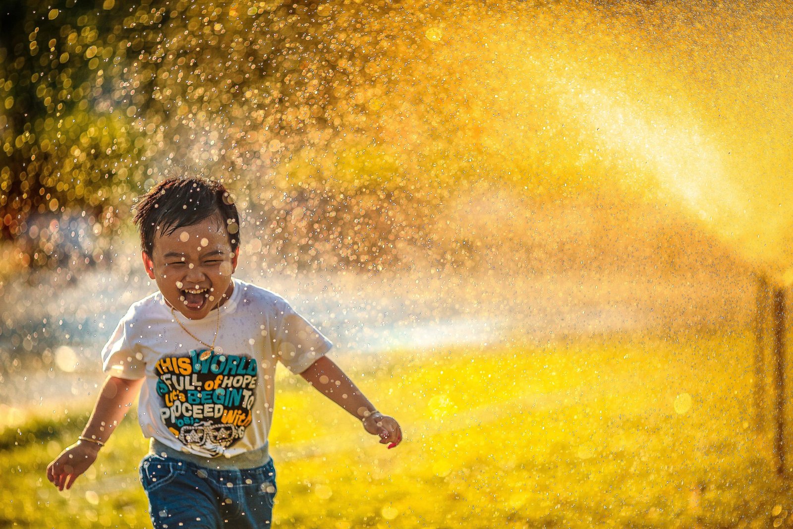 smiling child running through the sprinklers with fresh grass behind
