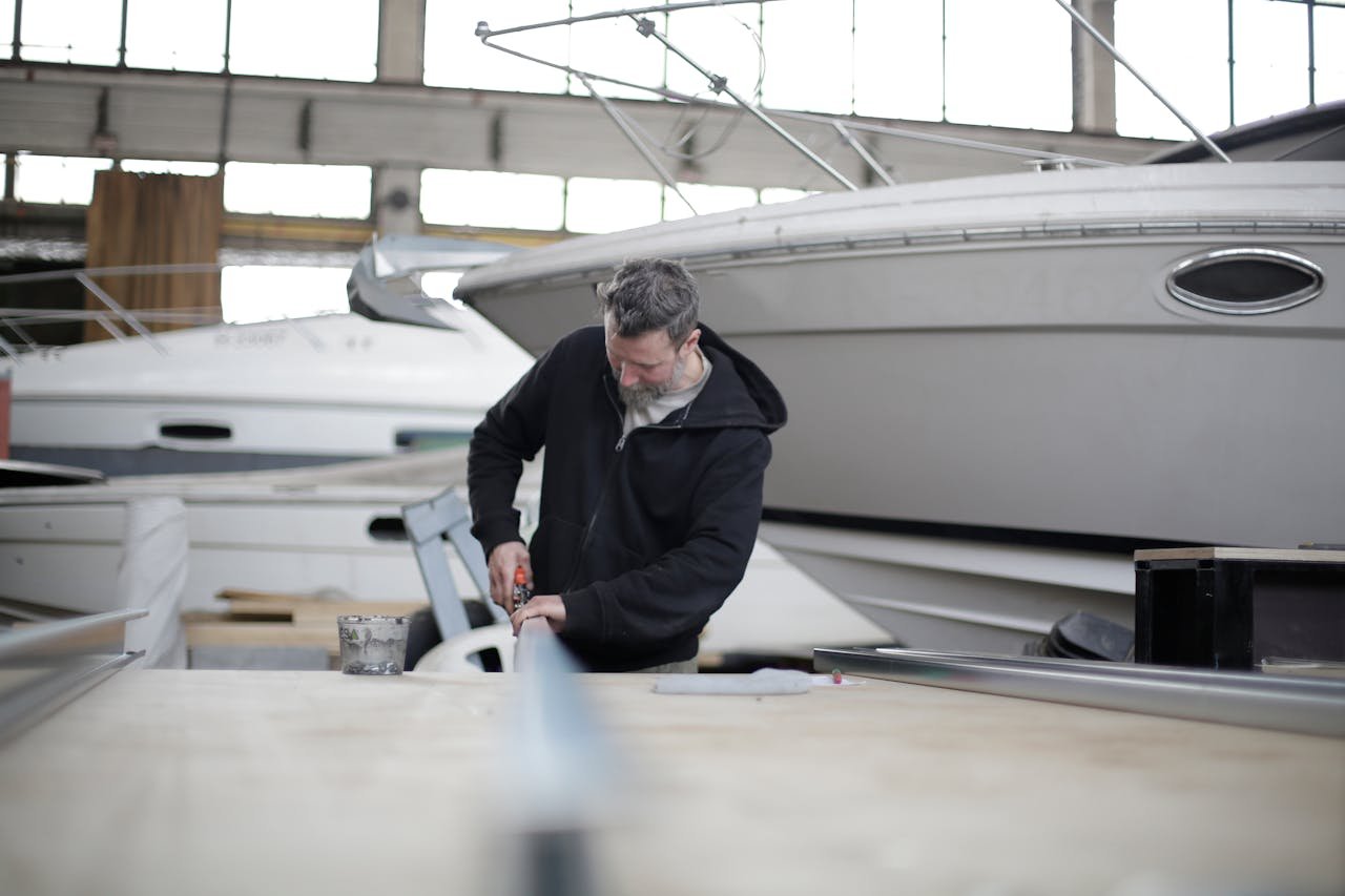 A mechanic is working with metal in front of the boat and thinking of shipping your boat across country.