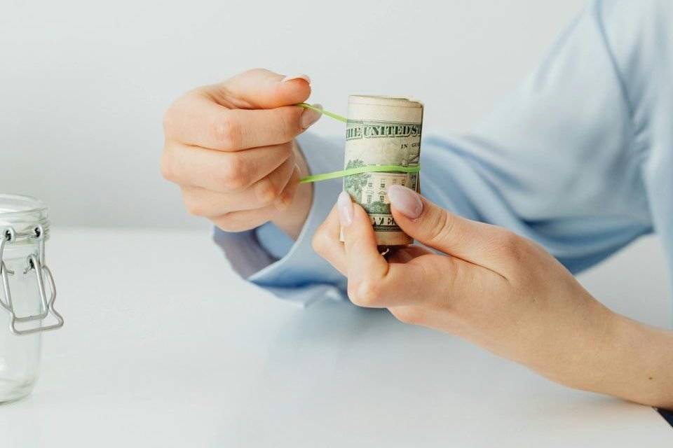 Hands putting a tie around dollar bills that are rolled up