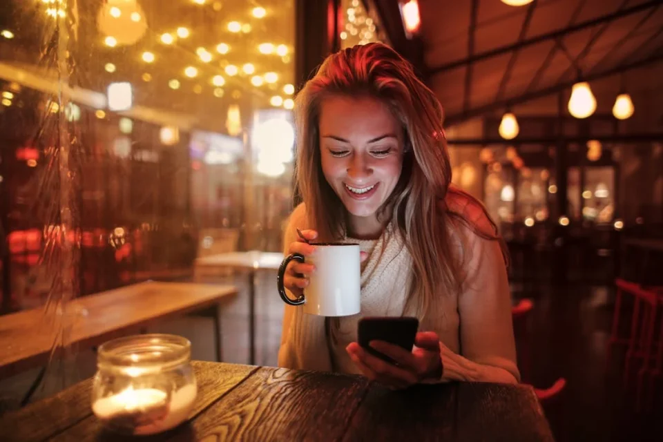 A smiling young woman sitting in a cafe and looking at her phone