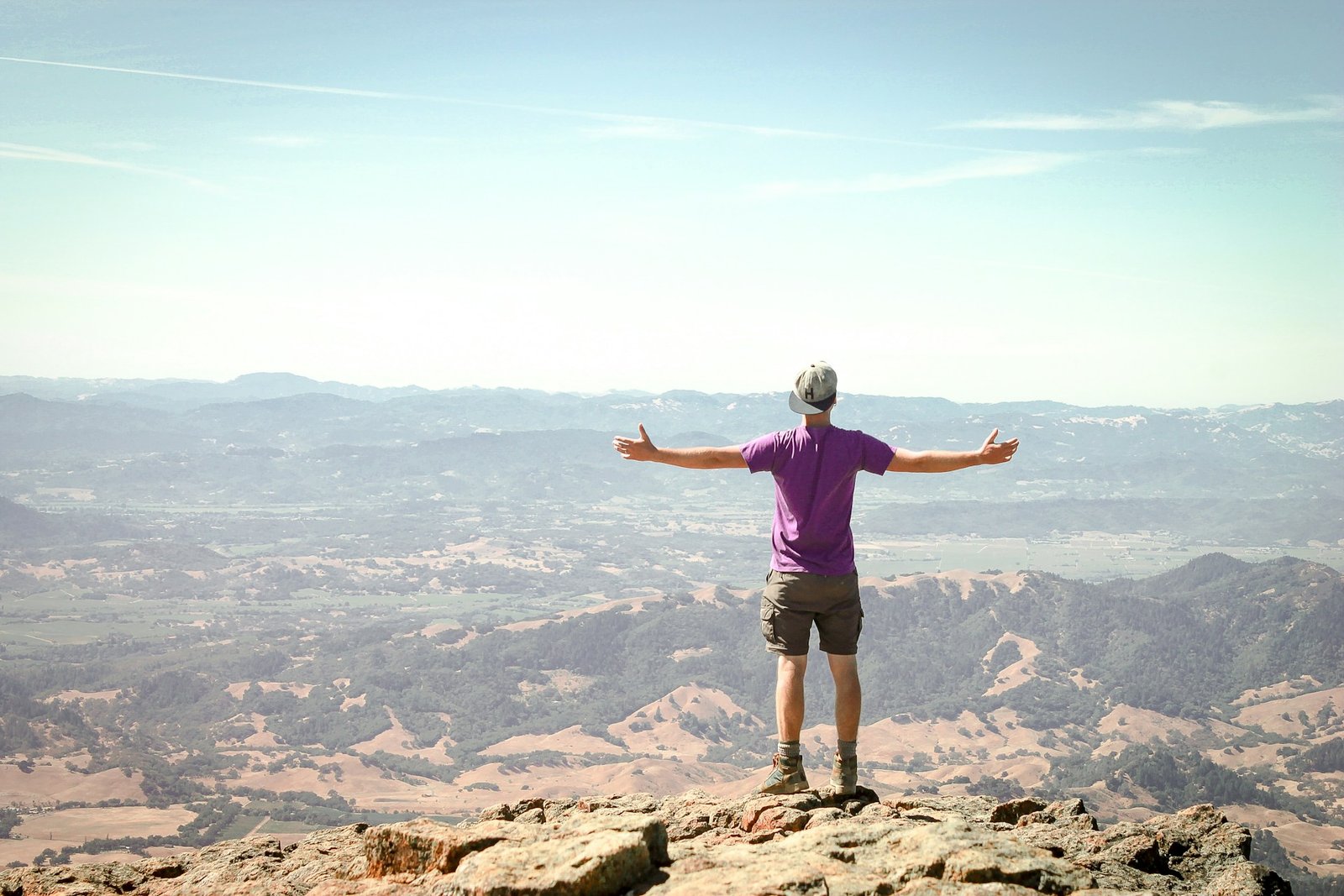 a man stands on top of a mountain with outstretched arms looking down into the valley