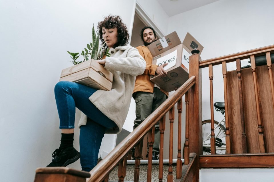 Man and woman carrying boxes and plants down the stairs