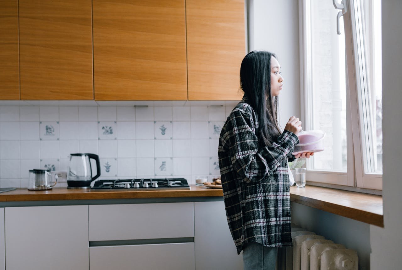 a woman in a plaid shirt looks out the kitchen window