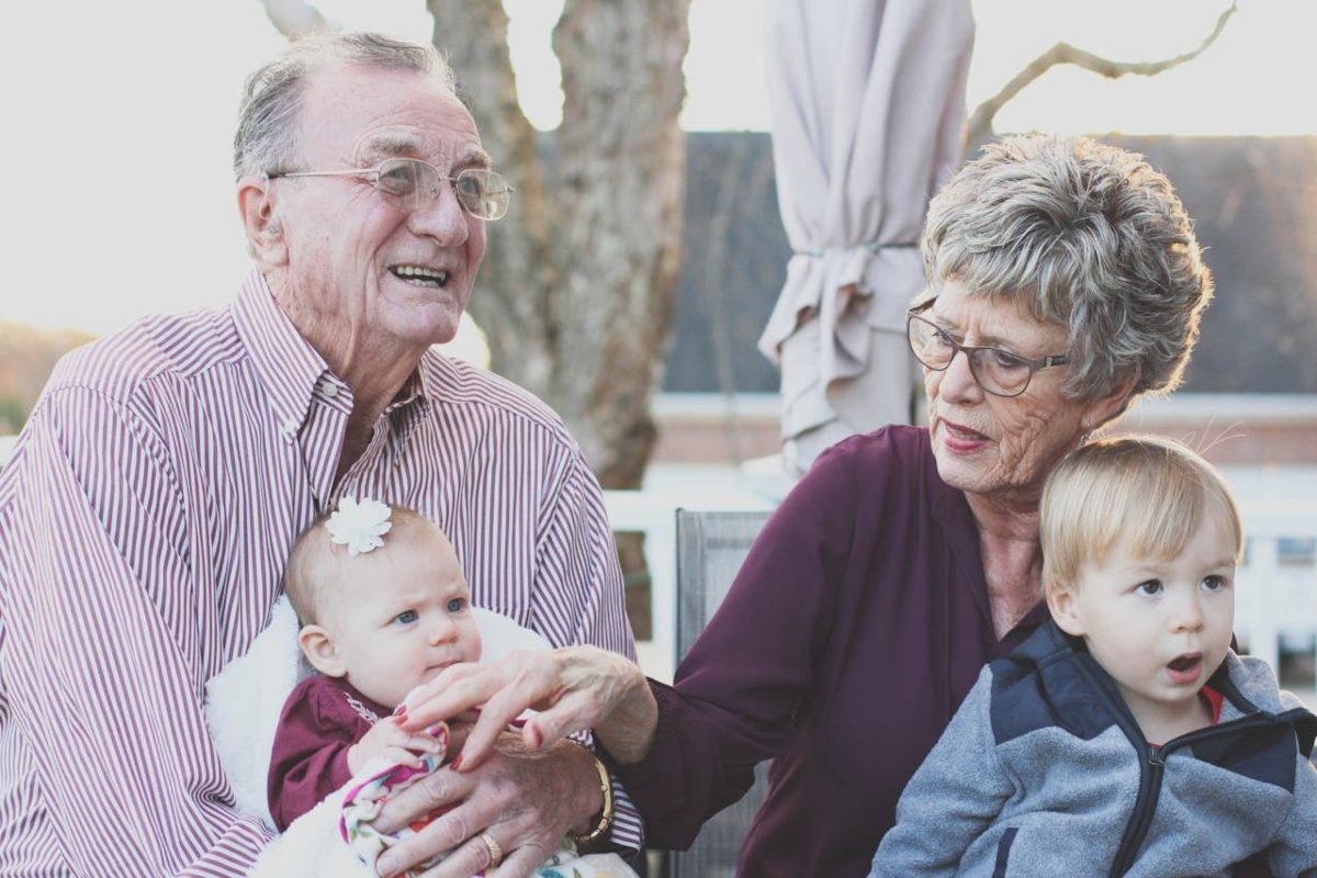 A pair of seniors, seated outdoors, gently interact with their two young grandchildren, creating a warm and loving family moment. Top senior living communities in Monterey County.