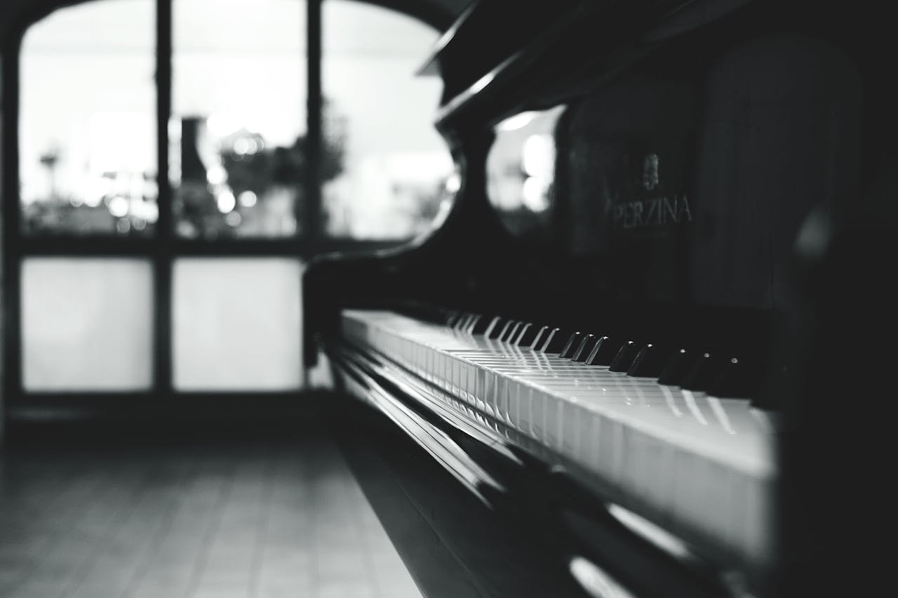 A close-up of a black piano's white keys, softly illuminated, with blurred windows in the background, creating a tranquil ambiance.